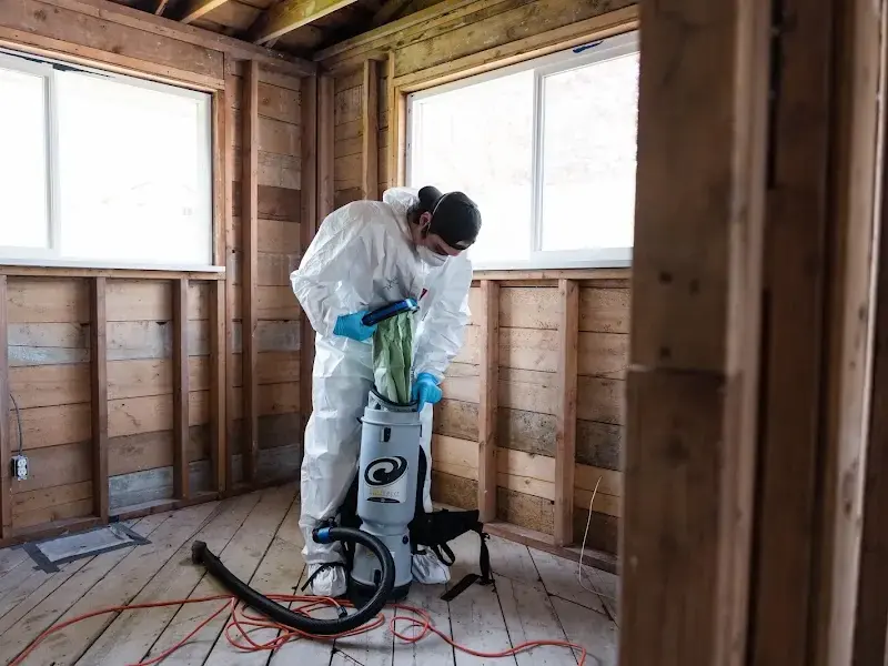 Technician in coveralls vacuuming a room stripped to the studs, shown for Arlington
