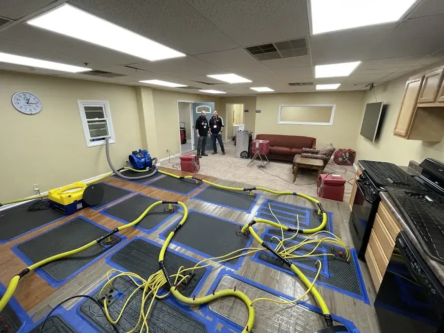 Drying mats, yellow hoses and air movers covering a wood floor in a large room