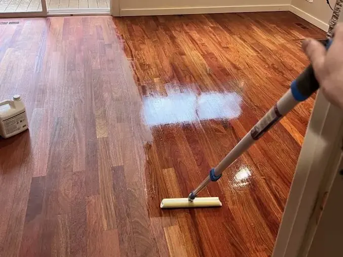 Squeegee pushing standing water across a hardwood floor in a sunlit room