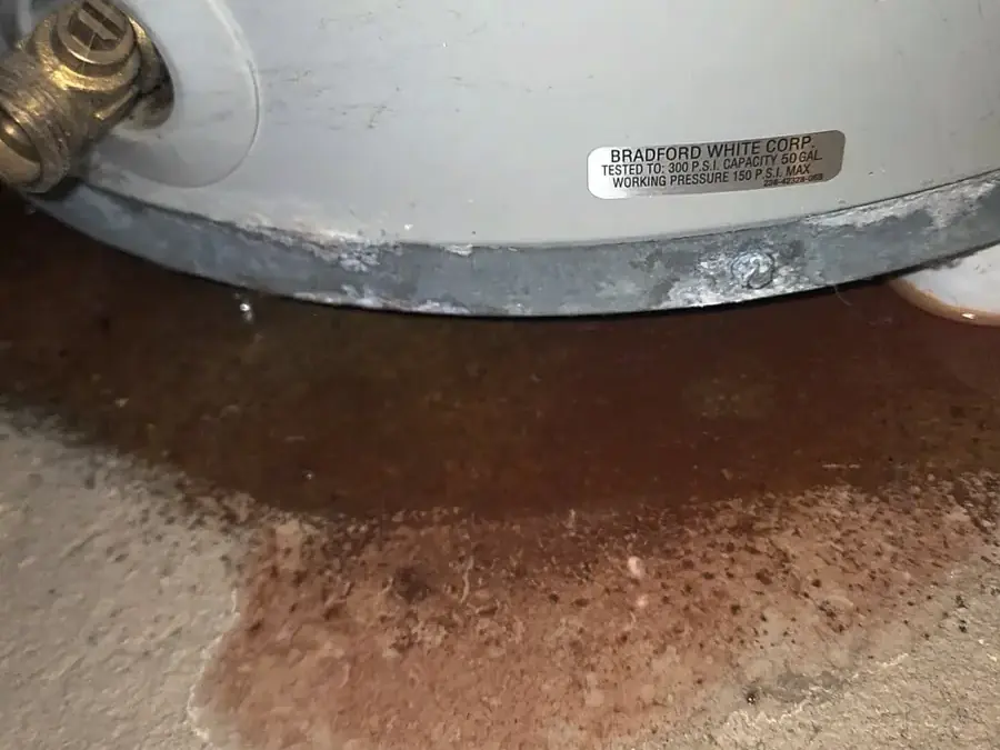 Rust-colored water pooled on concrete around the base of a water heater tank